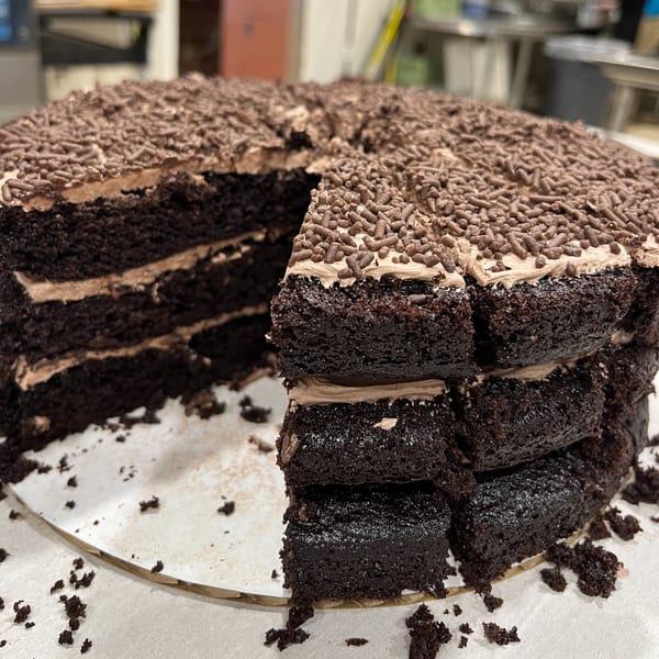 A large, round chocolate cake with chocolate frosting and sprinkles, with a slice removed.
