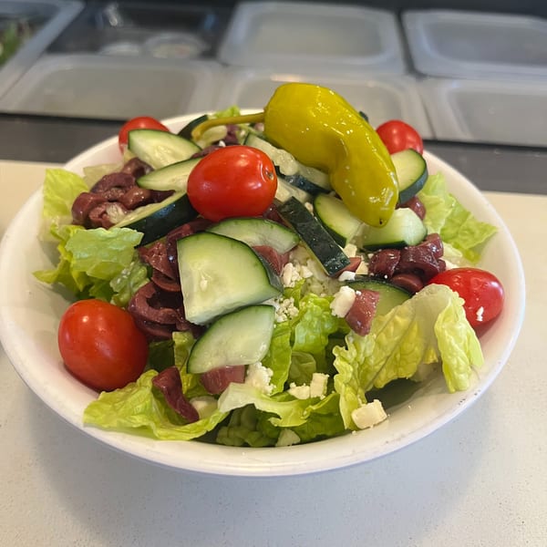 A fresh Greek salad with lettuce, tomatoes, cucumbers, olives, feta, and a pepperoncini.