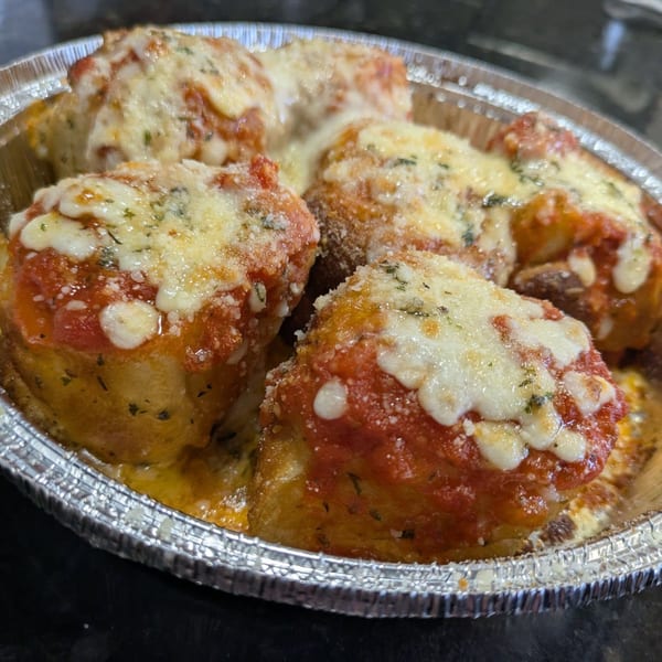 Close-up of Bodacious Pizza & Grill's baked pasta rolls with melted cheese and marinara sauce in a foil container.