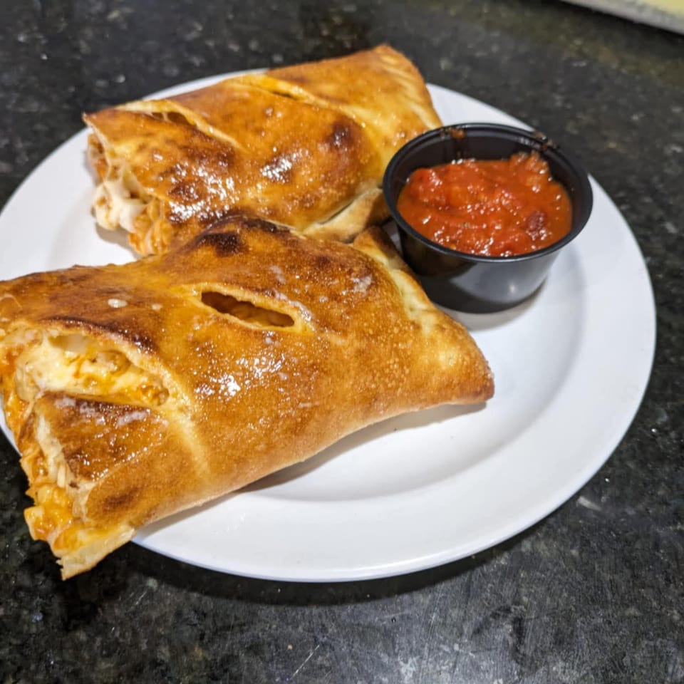 Two golden-brown calzones with cheese filling and a side of marinara sauce on a white plate.