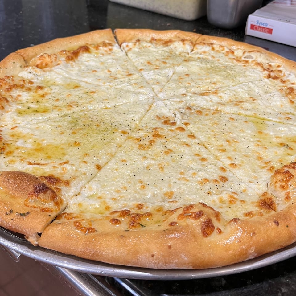 A freshly baked, sliced white pizza with melted cheese, herbs, and black pepper on a metal pan.